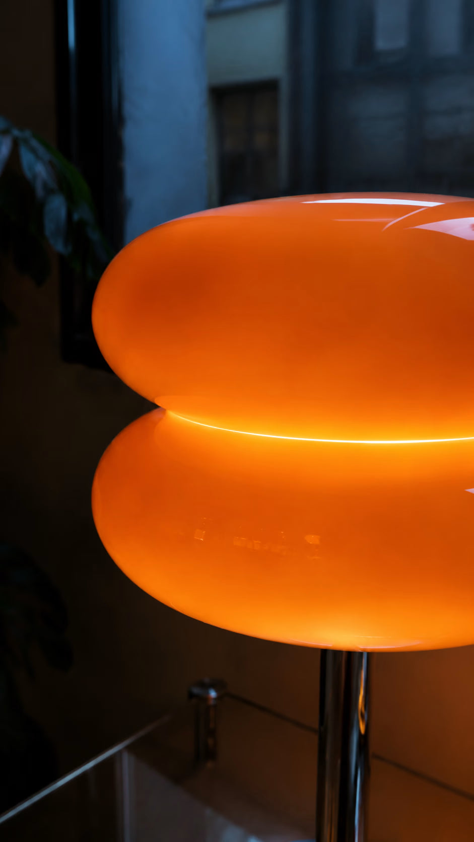 Macaron orange table lamp glowing beside a sofa in a warm interior