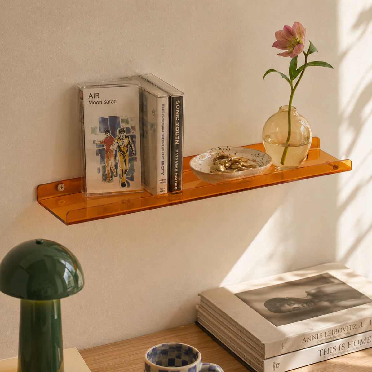 Orange acrylic wall shelf holding music cases, jewellery and a glass vase